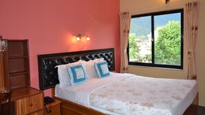 A bedroom with a large bed, a wooden nightstand, a bedside table, and a window with curtains. - Ranss Apartment (Pokhara)
