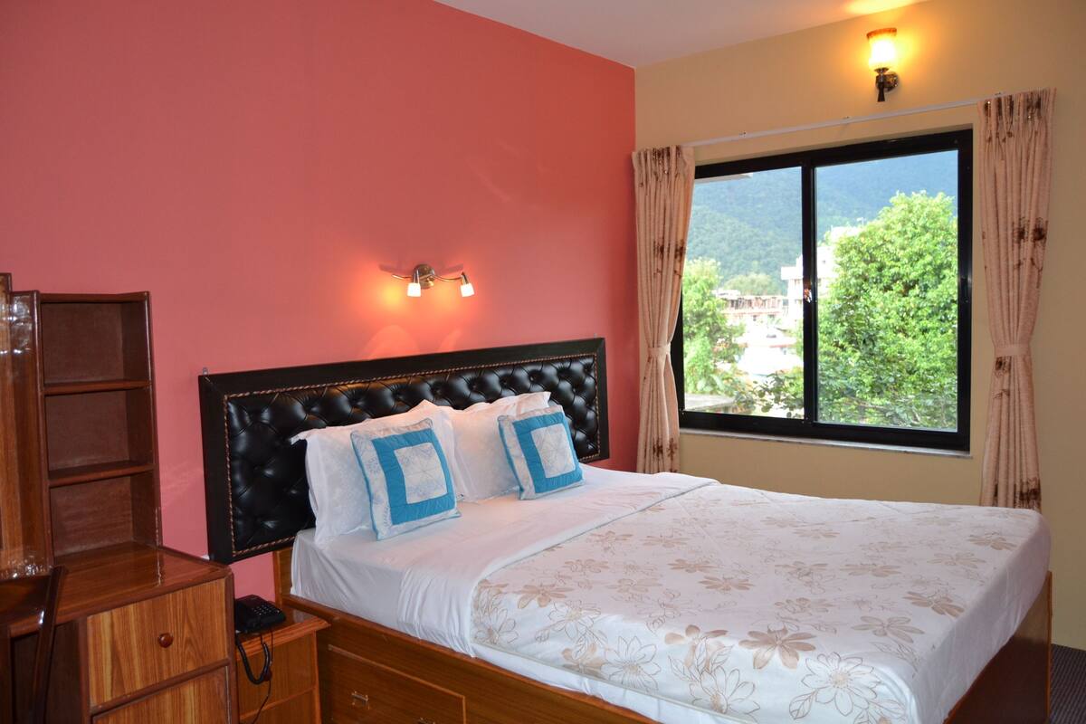 A bedroom with a large bed, a wooden nightstand, a bedside table, and a window with curtains.