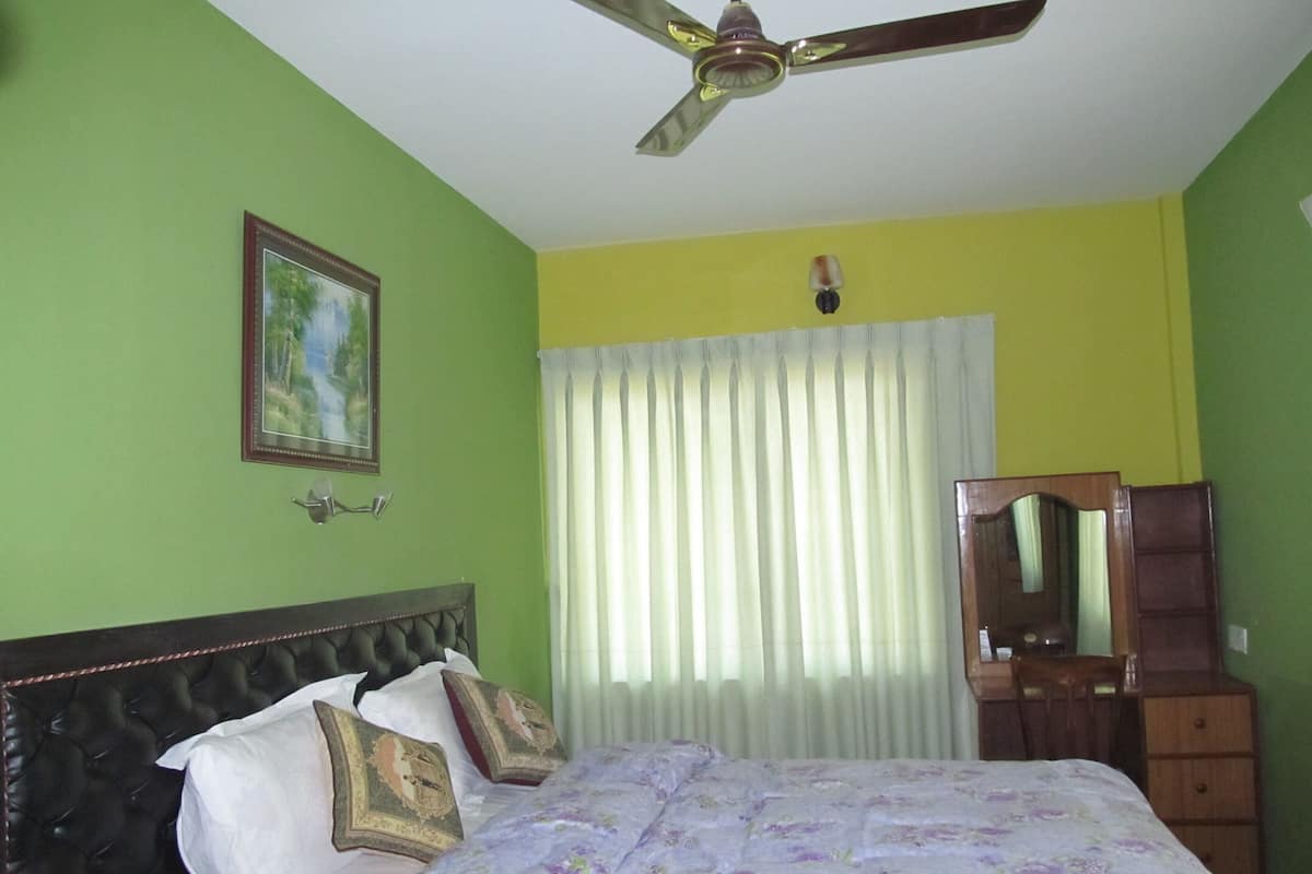 A bedroom with a bed, a ceiling fan, a mirror, and a window with curtains.