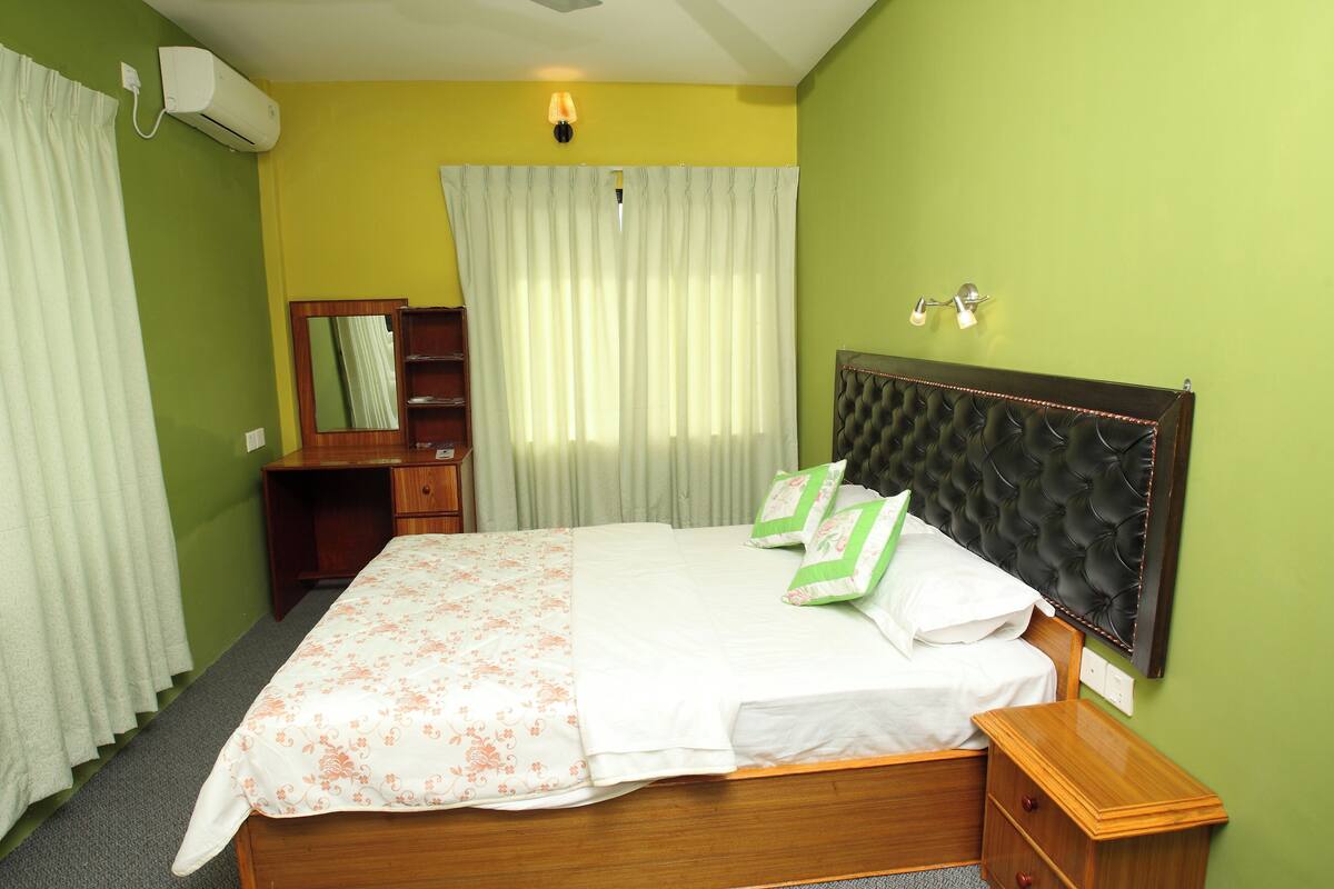 A bedroom with a bed, a nightstand, a dresser, a mirror, and a window with curtains.