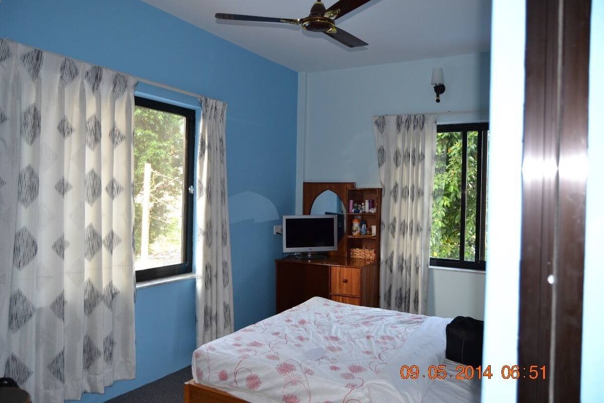 A bedroom with a bed, a television on a wooden cabinet, and curtains on the windows.