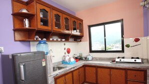 A kitchen with wooden cabinets, a refrigerator, and a window with a view. - Ranss Apartment (Pokhara)