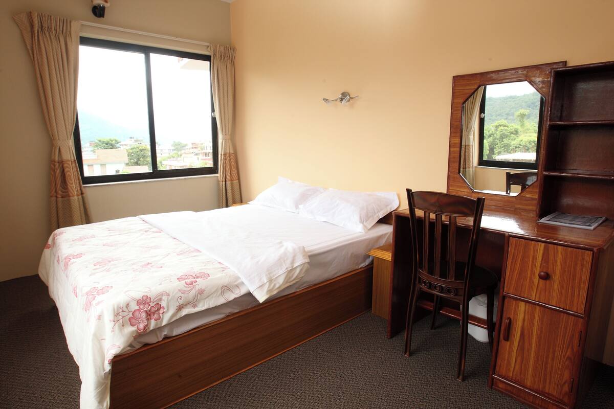 A bedroom with a bed, a desk, a chair, a mirror, and a window with curtains.