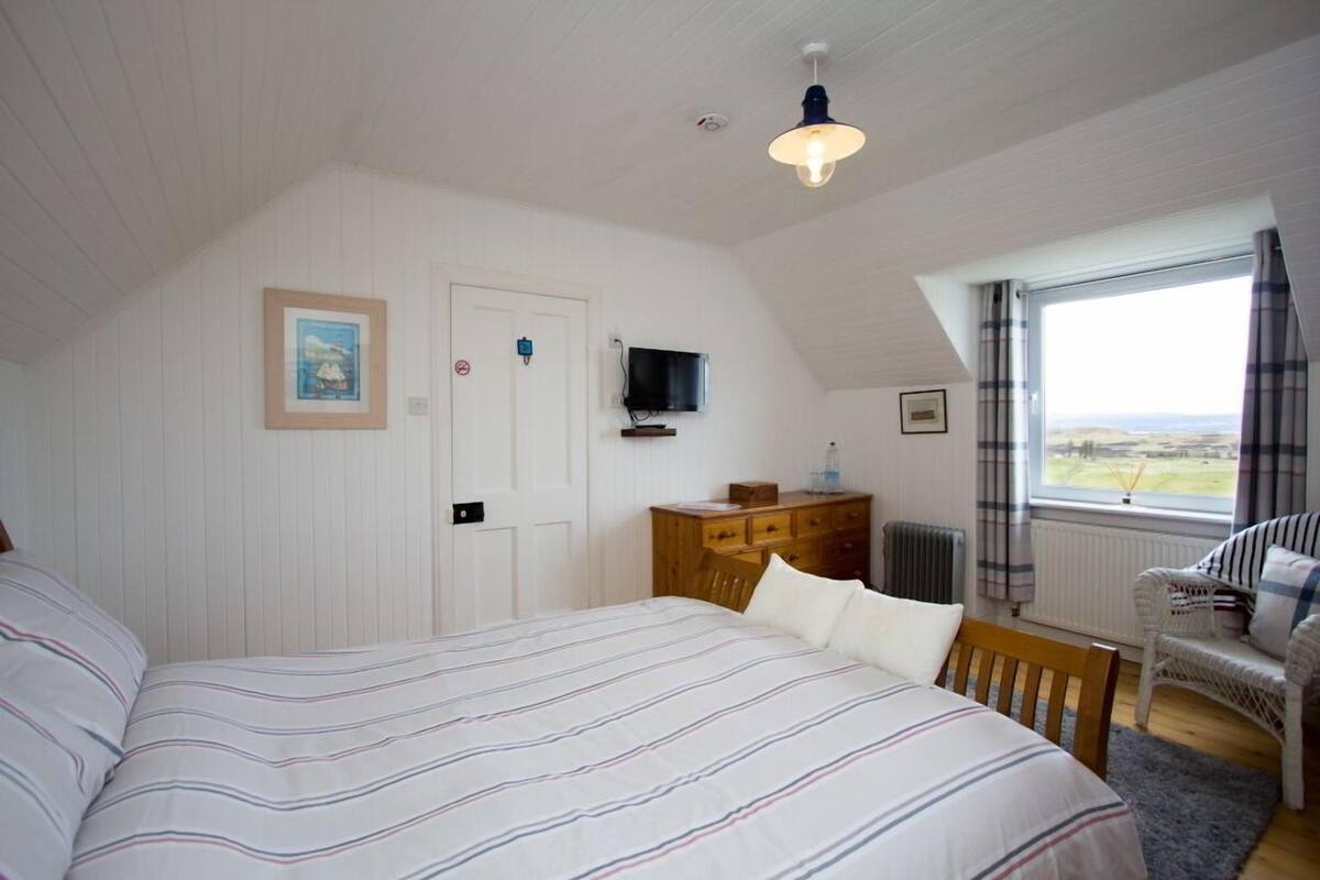 A bedroom with a large bed, a wooden dresser, a television, and a window with a view.