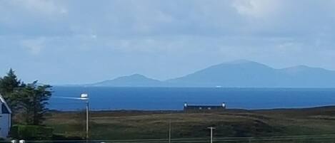 A coastal landscape with a body of water, a distant mountain range, and a few buildings.