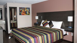 A hotel room with a large bed, two bedside tables with lamps, a mirror, and a colorful painting on the wall. - Castle Inn (Castleton-on-Hudson)