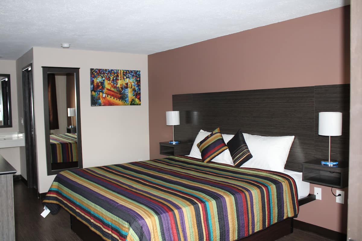 A hotel room with a large bed, two bedside tables with lamps, a mirror, and a colorful painting on the wall.