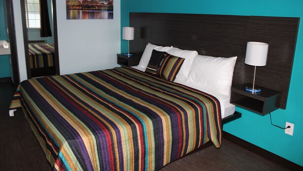 A hotel room with a large bed, a nightstand, a lamp, and a wall-mounted shelf. - Castle Inn (Castleton-on-Hudson)
