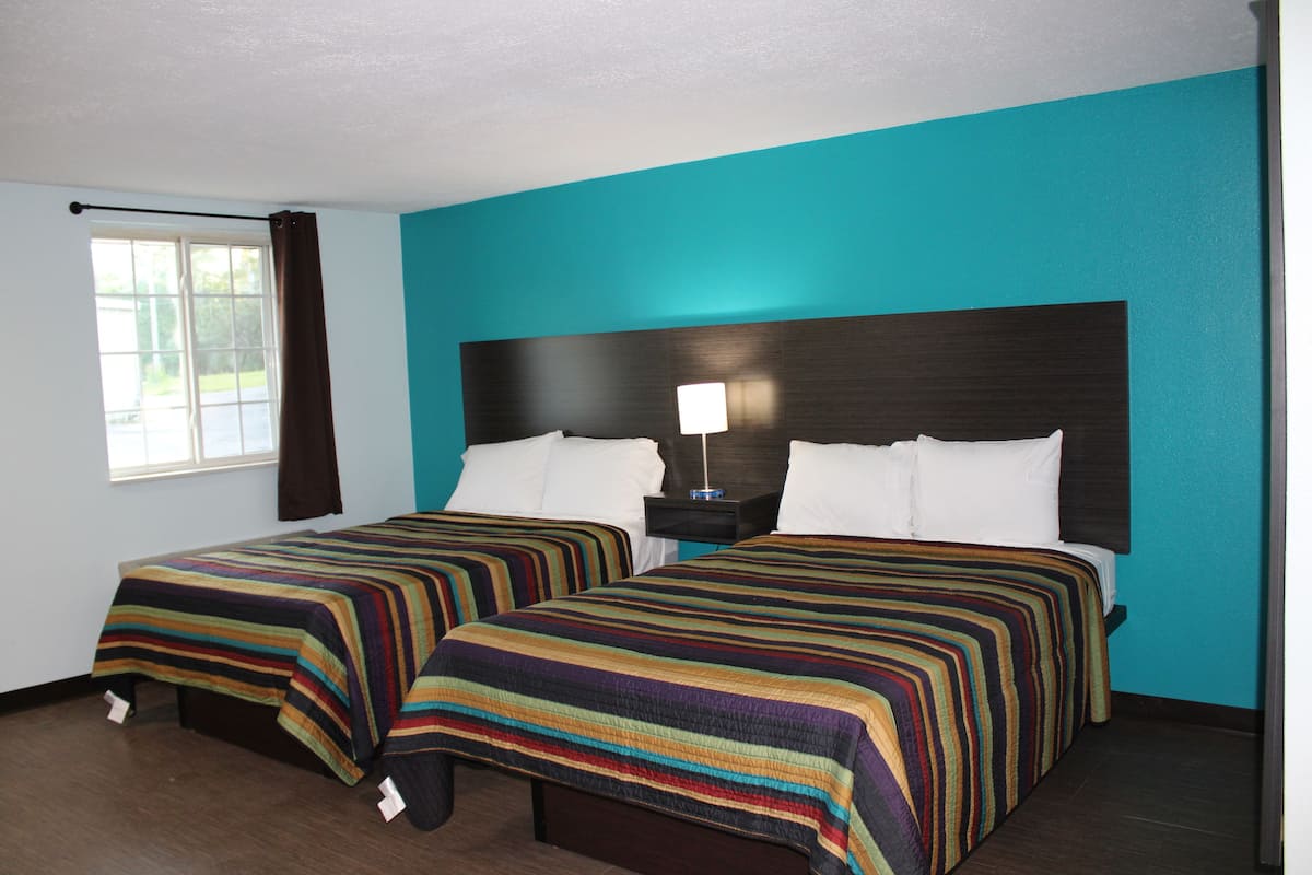 A hotel room with two beds, teal walls, and a window with curtains.