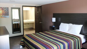 A hotel room with a bed, a nightstand, a lamp, a bathroom visible through an open door, and a painting on the wall. - Castle Inn (Castleton-on-Hudson)