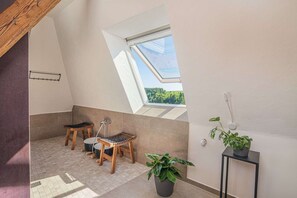 A small, sunlit room with a skylight, a wooden stool, a potted plant, and a black side table. - Modern Apartment with lift up, for 4 pers, 1 bedroom, 1 couch, historical building (Dornstetten)