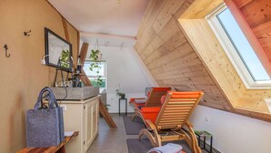 A cozy attic room with a sloped ceiling, wooden beams, a small kitchenette, and two wooden chairs with cushions.