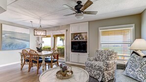 Un salon avec une table basse ronde, un fauteuil à motifs, un téléviseur et un ventilateur de plafond.