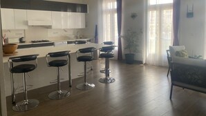 A modern kitchen with white cabinets, a central island with bar stools, a stove, and a sink. - Large apartment on canal 2 steps from downtown Sète (Sète)