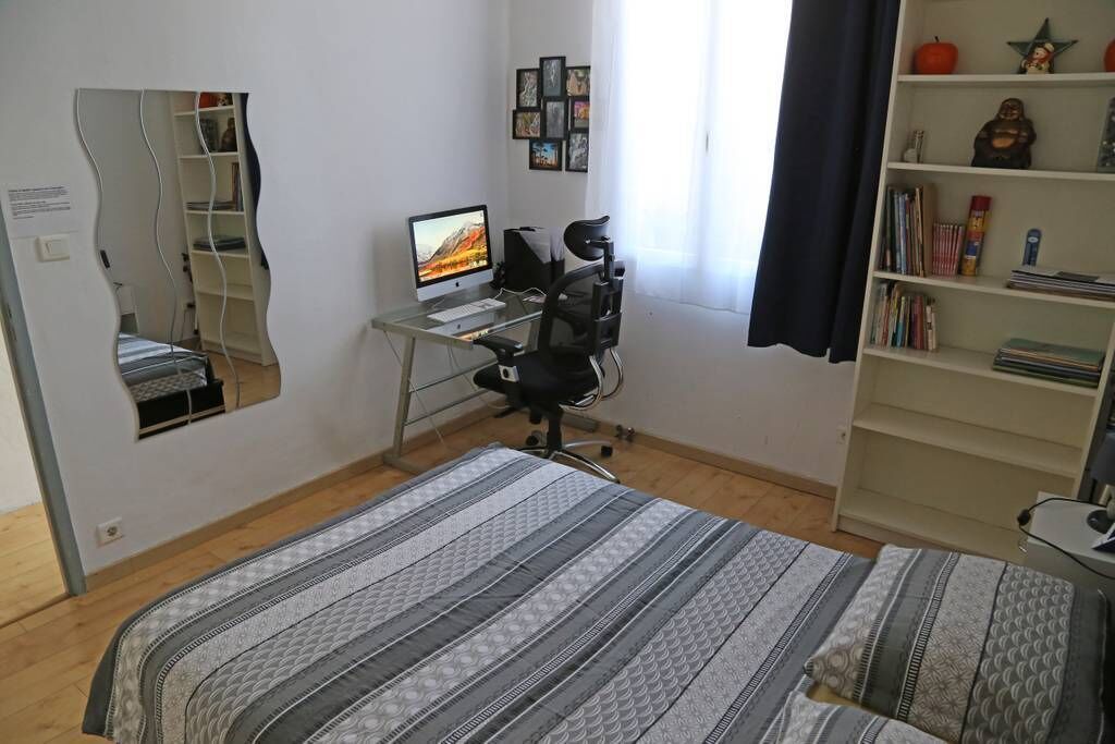 A bedroom with a bed, a desk with a computer, a chair, a bookshelf, and a mirror.