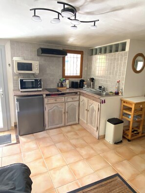 Cocina compacta con refrigerador, microondas y horno tostador. Hay una ventana con barrotes, un lavamanos y un bote pequeño de basura.