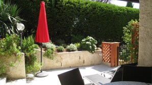 Een terras buiten met een rode parasol, een stenen muur en diverse planten.