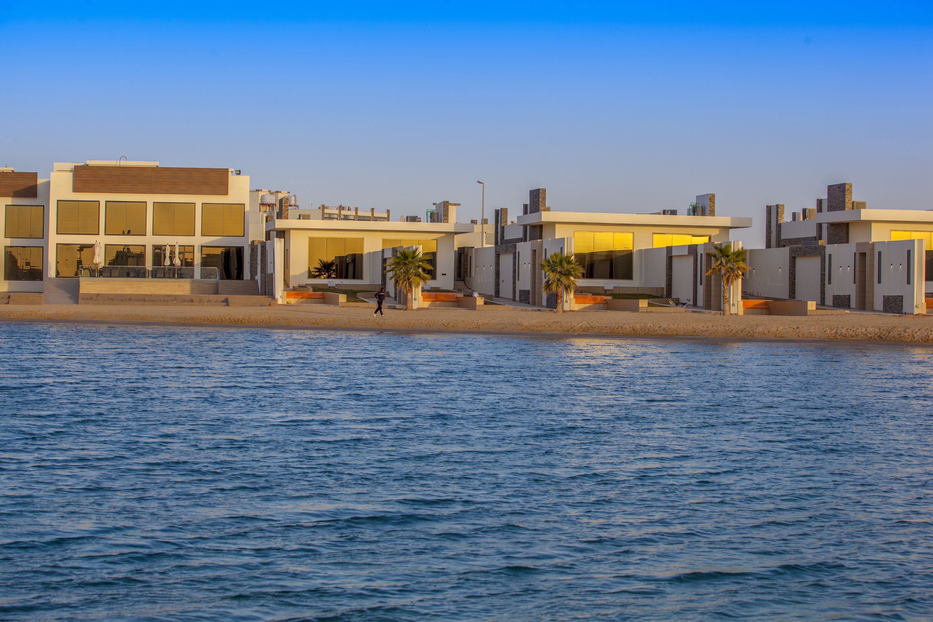 Een kusthotel met moderne architectuur, bestaande uit meerdere gebouwen met grote ramen en balkons met uitzicht op zee.
