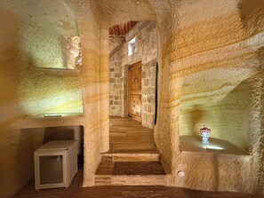 A narrow stone corridor with wooden steps leading to a door, shelves with decorative items, and a small cabinet. - Crassus Cave Hotel (Ürgüp)