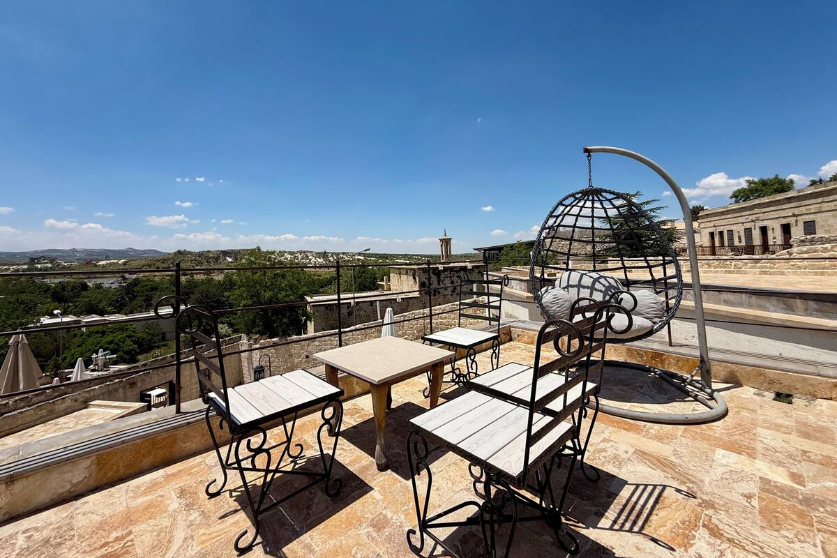 Una terraza en la azotea con mobiliario exterior, una silla colgante y vistas del paisaje circundante.