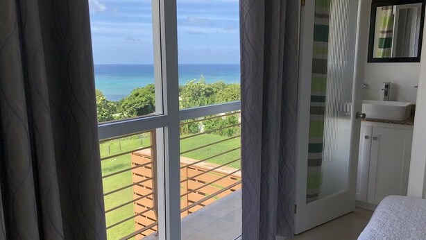 A bedroom with a view of the ocean, a balcony with a wooden deck, and a bathroom with a sink and mirror.