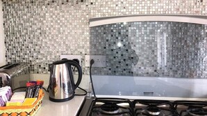 A kitchen with a gas stove, a kettle, and a toaster. There is a basket of snacks and a box of tissues on the counter.