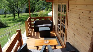 Une terrasse en bois aménagée avec du mobilier d’extérieur, comprenant un canapé et deux fauteuils, ainsi qu’une table agrémentée d’un centre de table en verre.