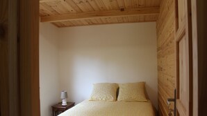 Une chambre à coucher avec un lit, deux oreillers, une table de chevet avec une lampe, et des panneaux de bois aux murs et au plafond.
