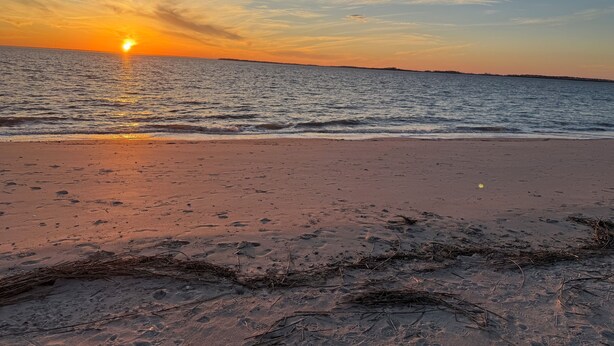 Ein Strand bei Sonnenuntergang, ruhiges Meer und eine entfernte Küste.
