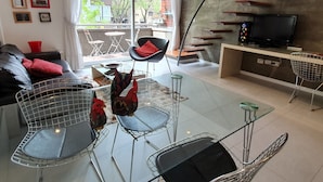 A modern living room with a glass dining table, two chairs, a sofa, a TV, and a balcony with outdoor furniture. - LUXURY DUPLEX, fully equipped, 2Bd, pool & terrace (Palermo)