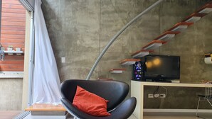 A modern living room with a black chair, a television, and a concrete wall. - LUXURY DUPLEX, fully equipped, 2Bd, pool & terrace (Palermo)