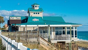 Un edificio frente a la playa con un letrero que dice "Capt. Dave's on the Gulf", un símbolo de pez y un balcón con vista al océano.