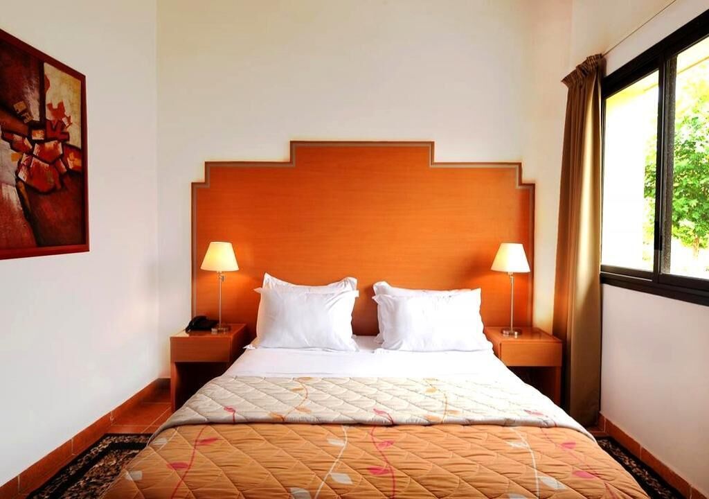 A hotel room with a large bed, two bedside lamps, a wooden headboard, and a window with curtains.