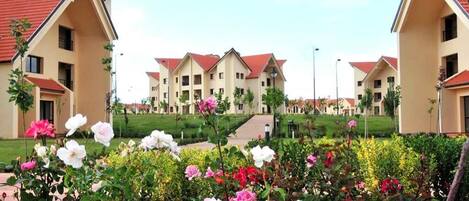 A residential building complex with multiple apartment buildings, a central pathway, and a well-maintained garden with various flowers.
