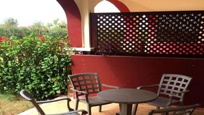 Een terras buiten met een ronde tafel en vier stoelen, een rode muur en een lattenhek.