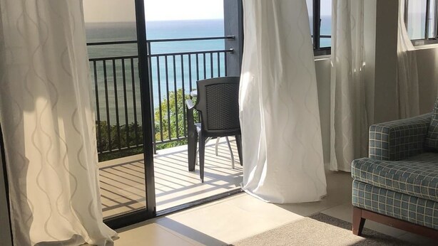 A room with a view of the ocean through a sliding glass door, a black chair, and a patterned sofa. - Calabash Villas on Bonaire Bay (Gros Islet)
