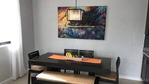 A dining area with a dark wooden table, cushioned benches, and a colorful painting above. - Calabash Villas on Bonaire Bay (Gros Islet)