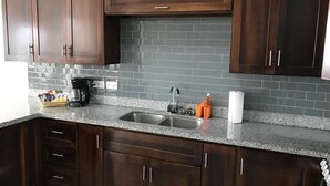 A kitchen with dark wooden cabinets, a granite countertop, a double sink, and a tiled backsplash. - Calabash Villas on Bonaire Bay (Gros Islet)