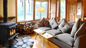 A cozy living room with a wood-burning stove, a sofa, a coffee table, and a stone fireplace surround. - Chalet Sean, peaceful retreat on beautiful mountain brook and walk to river.. (Sutton)