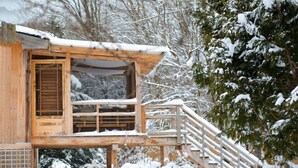 A wooden cabin with a balcony and a staircase leading to a deck, surrounded by snow-covered trees. - Chalet Sean, peaceful retreat on beautiful mountain brook and walk to river.. (Sutton)