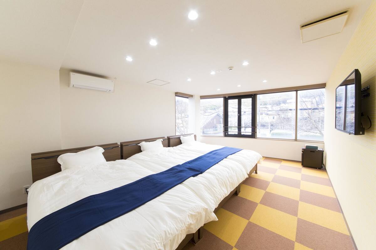 Una habitación de hotel con una cama grande, piso a cuadros, una ventana con vista y un televisor montado.