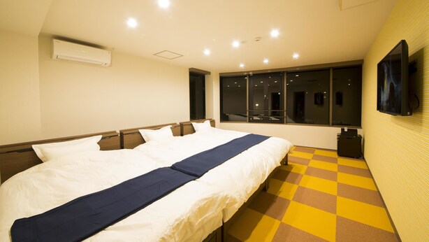 Habitación de hotel con una cama grande, un televisor de pantalla plana montado en la pared y un ventanal con vistas al exterior.