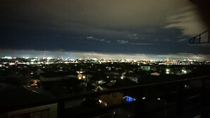 Panorama nocturno de una ciudad con vista a una zona densamente poblada y una torre distante.