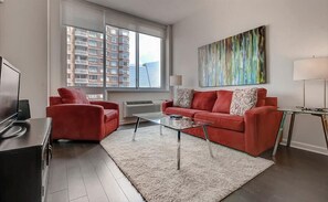 Uma sala de estar moderna com um sofá vermelho, uma mesa de centro de vidro e uma janela ampla com vista para um edifício alto.
