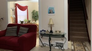 Een woonkamer met een rode bank, een glazen salontafel en een trap naar een andere kamer.