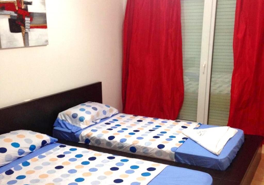 Une chambre avec deux lits, chacun recouvert d’une couvre-lit à pois, avec des rideaux rouges et un miroir au mur.