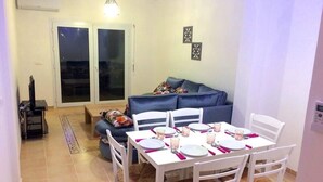 A dining area with a white table set for four, white chairs, and a blue sofa in the background. - Residence Marina Saidia 4246 (Saidia)