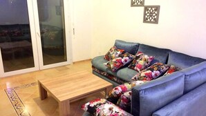 A living room with a blue sofa, floral cushions, a wooden coffee table, and a sliding glass door leading to an outdoor area. - Residence Marina Saidia 4246 (Saidia)
