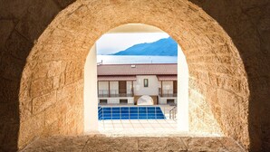 Une structure en pierre en forme d’arc, d’où l’on peut admirer un bâtiment doté d’un toit en tuiles et d’une piscine.