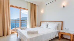 Une chambre d’hôtel avec un grand lit, une table de chevet en bois, une fenêtre avec des rideaux et une vue sur la mer.